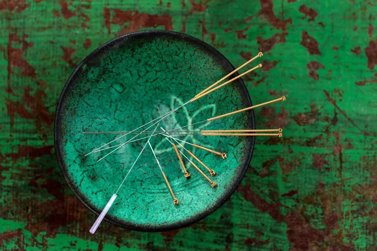 Acupuncture needles with gold handles resting in a green ceramic bowl